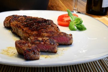 Mariniertes Steak auf einem weißen Teller dekoriert mit einer Tomatenscheibe und Basilikumblättern.